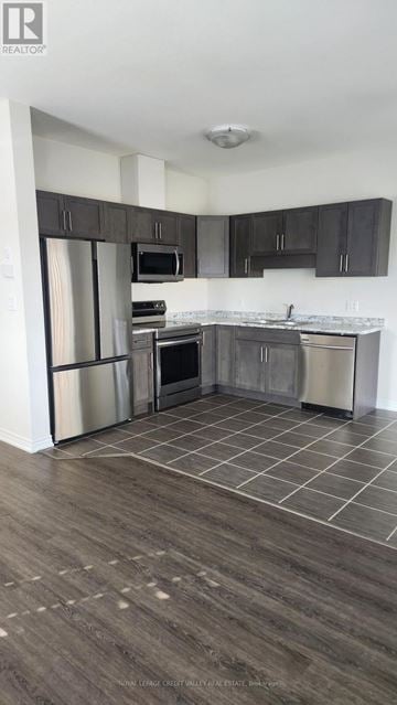 Welland (West Welland) townhouse for rent - A kitchen with a refrigerator, microwave, oven, and cabinets.