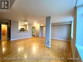 Toronto (Waterfront Communities) condo for rent - A spacious room with wooden flooring and white walls, with a kitchen area visible in the background.