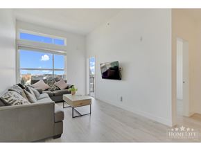 Langley apartment for rent - A living room with a grey couch, a coffee table, and a large window with a view of the city.