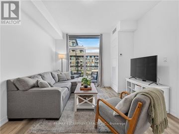 Hamilton (Waterdown) condo for rent - A living room with a grey couch, a wooden chair, and a television on a white stand.
