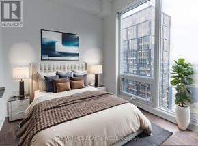 Toronto (Waterfront Communities) condo for rent - A bedroom with a large bed, a potted plant, and a view of a cityscape through a window.