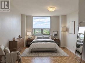 Toronto (Eglinton East) condo for rent - A bedroom with a large bed, a nightstand, a chair, and a window with a view of the sky.