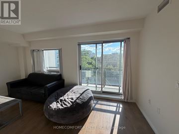 Waterloo condo for rent - A living room with a black couch and a round ottoman in front of a large window.