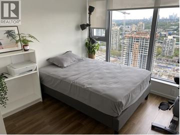 Burnaby apartment for rent - A bedroom with a large bed and a window overlooking a cityscape.