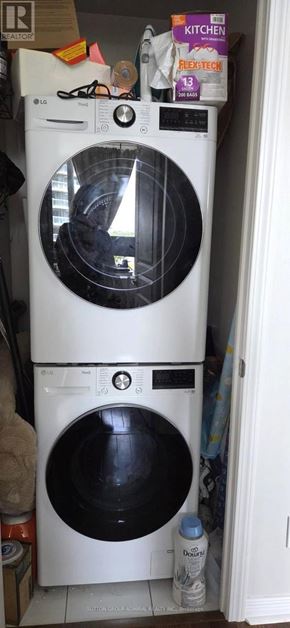 Toronto (Mimico) condo for rent - A white washing machine with a black door is in a cluttered kitchen.