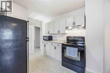 Sarnia apartment for rent - A black refrigerator is in a kitchen with white cabinets and a black stove.