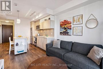 Toronto (Henry Farm) condo for rent - A living room with a grey couch and a kitchen area in the background.