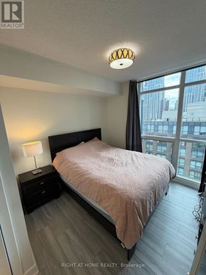 Toronto (Church-Yonge Corridor) condo for rent - A bedroom with a bed, nightstand, and window overlooking a cityscape.