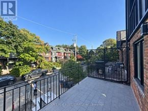 Toronto (University) apartment for rent - A balcony with a black railing overlooks a street with cars and houses.