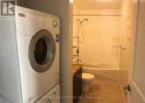 Toronto (Willowdale East) condo for rent - A white washing machine is in a small bathroom with a toilet and a walk-in shower.