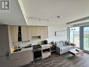 Mississauga (City Centre) condo for rent - A modern kitchen with a stove top oven and a grey couch.