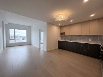 Vancouver apartment for rent - A spacious room with wooden floors and a kitchen area with black cabinets.