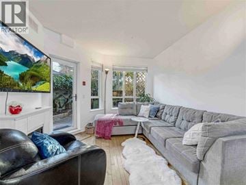 Vancouver apartment for rent - A living room with a grey couch, a black leather chair, and a television displaying a mountain landscape.