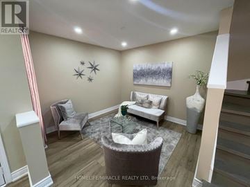 Brampton (Fletcher's Meadow) apartment for rent - A living room with a grey sofa, a white armchair, a glass coffee table, and a painting on the wall.