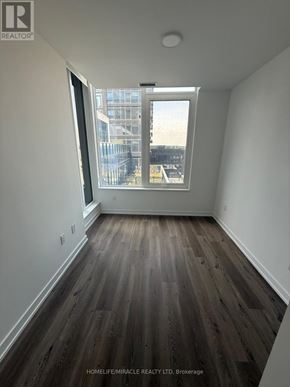 Mississauga (City Centre) condo for rent - A room with wooden flooring and a window overlooking a cityscape.