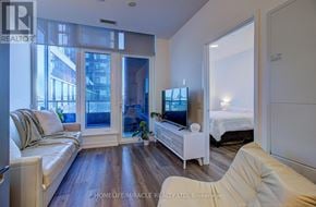 Mississauga (City Centre) condo for rent - A spacious room with wooden flooring and a kitchen area in the background.