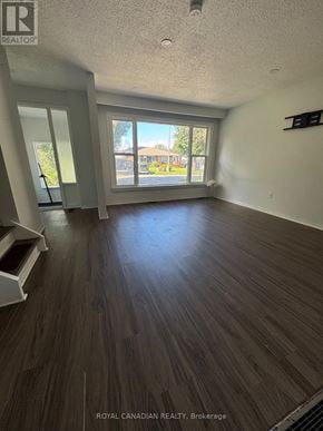 Oshawa (Vanier) apartment for rent - A spacious room with wooden flooring and a large window.