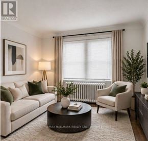 St. Catharines (Downtown) duplex for rent - A living room with a white sofa, a green cushion, a black coffee table, a white chair, a small potted plant, and a framed picture on the wall.