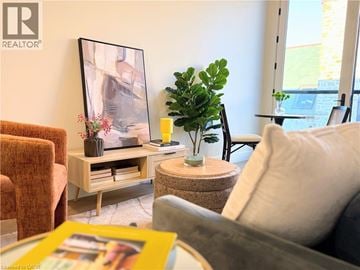 Hamilton apartment for rent - A living room with a grey couch, a brown chair, a wooden coffee table with a vase and a plant on it, and a framed picture on the wall.