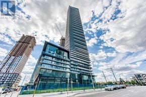 Mississauga (City Centre) condo for rent - A modern building with a unique curved glass facade stands tall against a partly cloudy sky.