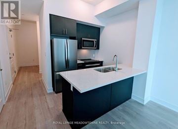 Hamilton (Waterdown) condo for rent - A kitchen with a black fridge and microwave, a white counter top, and a sink.