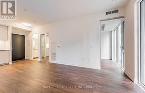 Toronto (Moss Park) condo for rent - A spacious room with wooden flooring and white walls, with a door on the left and a window on the right.