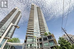 Toronto (Mimico) condo for rent - A tall residential building with a glass facade stands under a blue sky with clouds.