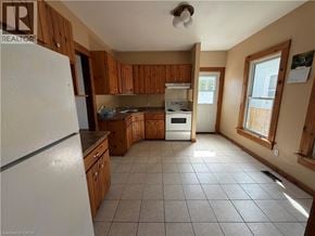 Niagara Falls apartment for rent - A kitchen with a white fridge, wooden cabinets, and a tiled floor.