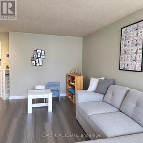 Brampton (Queen Street Corridor) condo for rent - A living room with a grey couch, a white table, and a wall with a picture of a family.