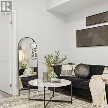 Niagara Falls (Arad/Fallsview) townhouse for rent - A living room with a black couch, a round mirror, and a coffee table with a vase of flowers on it.