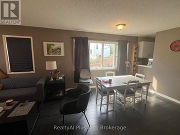 Toronto (Birchcliffe-Cliffside) townhouse for rent - A living room with a grey couch, a black chair, and a dining table with chairs.