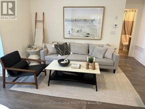 Pickering (Town Centre) townhouse for rent - A living room with a grey couch, a black chair, a white side table, and a framed picture on the wall.