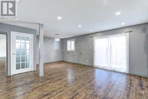 Brampton (Madoc) townhouse for rent - A spacious room with wooden floors and white walls, with a door on the left and a window on the right.