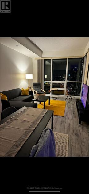 Toronto (Mimico) condo for rent - A modern living room with a black couch and a large window overlooking the city.