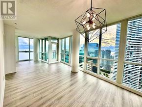 Toronto (Waterfront Communities) condo for rent - A large, empty room with wooden floors and a view of the city through the windows.