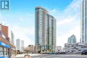 Mississauga (City Centre) condo for rent - A tall, curved glass building stands in the middle of a city street.