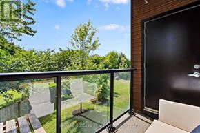 St. Catharines (Lakeport) condo for rent - A balcony with a glass railing and a white chair overlooking a green backyard.