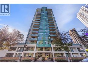 Coquitlam apartment for rent - A tall building with a glass facade stands in front of a tree and other buildings.