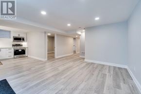 Mississauga (Lisgar) apartment for rent - A spacious room with wooden flooring and white walls, featuring a kitchen area with a stove and cabinets.