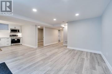 Mississauga (Lisgar) apartment for rent - A spacious room with wooden flooring and white walls, featuring a kitchen area with a stove and cabinets.