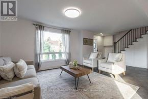 Quinte West (Trenton Ward) apartment for rent - A well-lit living room with a grey sofa, a wooden coffee table, and a staircase with a black railing.