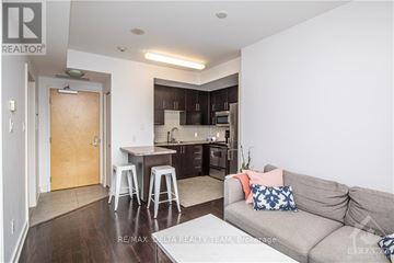 Ottawa apartment for rent - A living room with a grey couch and a kitchen area in the background.