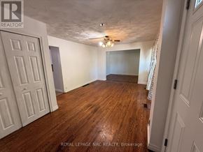 Niagara Falls (Ascot) apartment for rent - A room with wooden floors and white walls, with a ceiling fan and a door on the left.