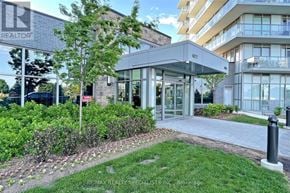 Mississauga (Central Erin Mills) condo for rent - A building with the number 4877 on it is surrounded by greenery.