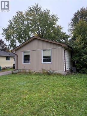 Waterloo apartment for rent - A small house with a brown siding and a grey roof is surrounded by green grass and trees.