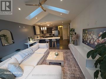 Toronto (South Riverdale) duplex for rent - A spacious living room with a white sofa and a kitchen in the background.