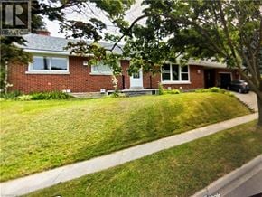 Kitchener apartment for rent - A house with a red brick exterior and a white door is surrounded by a green lawn.
