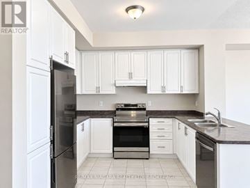 Thorold (Rolling Meadows) townhouse for rent - A kitchen with white cabinets and a black fridge.