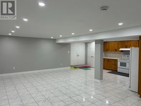 Toronto (West Hill) apartment for rent - A spacious, empty room with white tile flooring and a kitchen area with wooden cabinets and appliances.