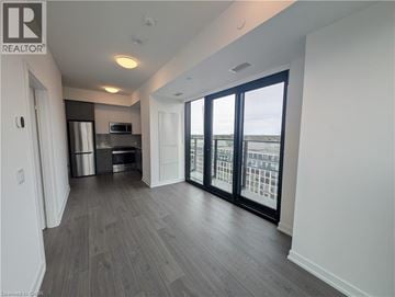 Kitchener condo for rent - A spacious room with a kitchen area and sliding glass doors leading to a balcony.